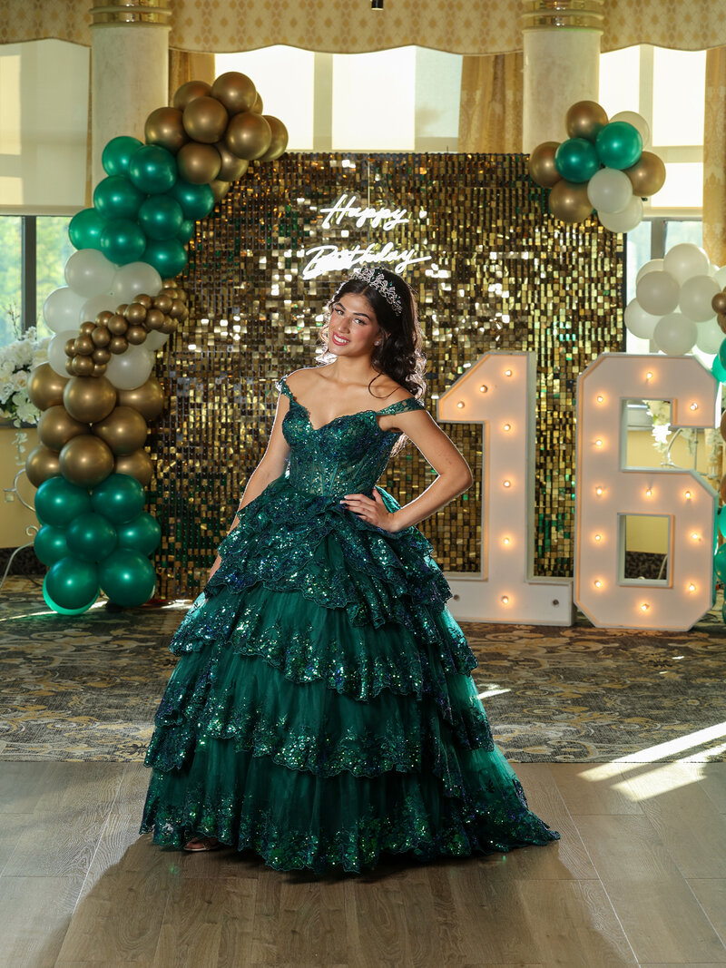 Girl in green dress standing in front of a large 16 with a happy birthday sign